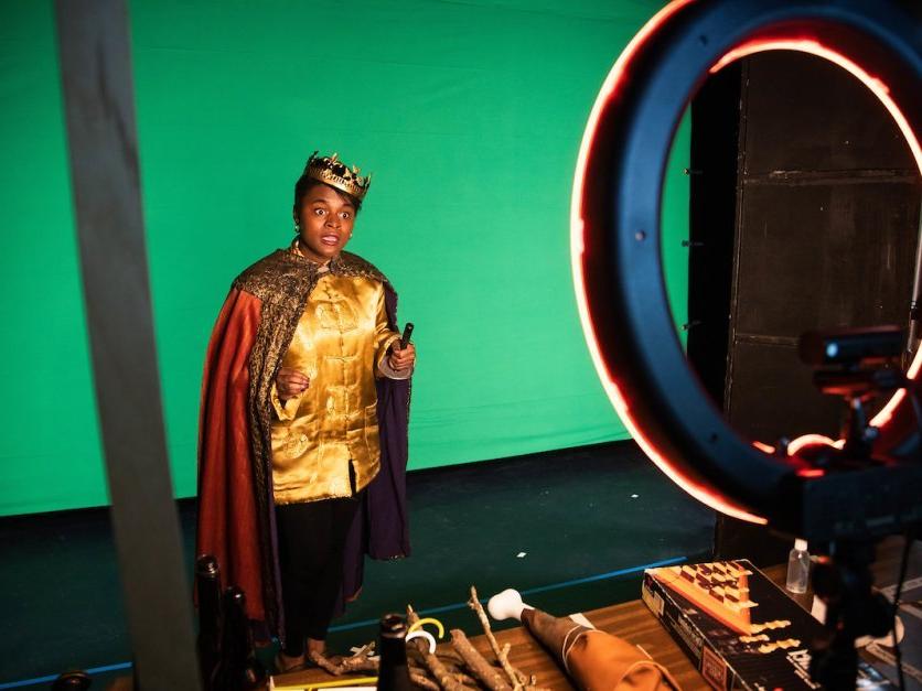 A student dressed in costume performs lines in front of a green screen